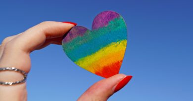 Photo of a person holding a multicolored heart deco. Happy Queer books reading!