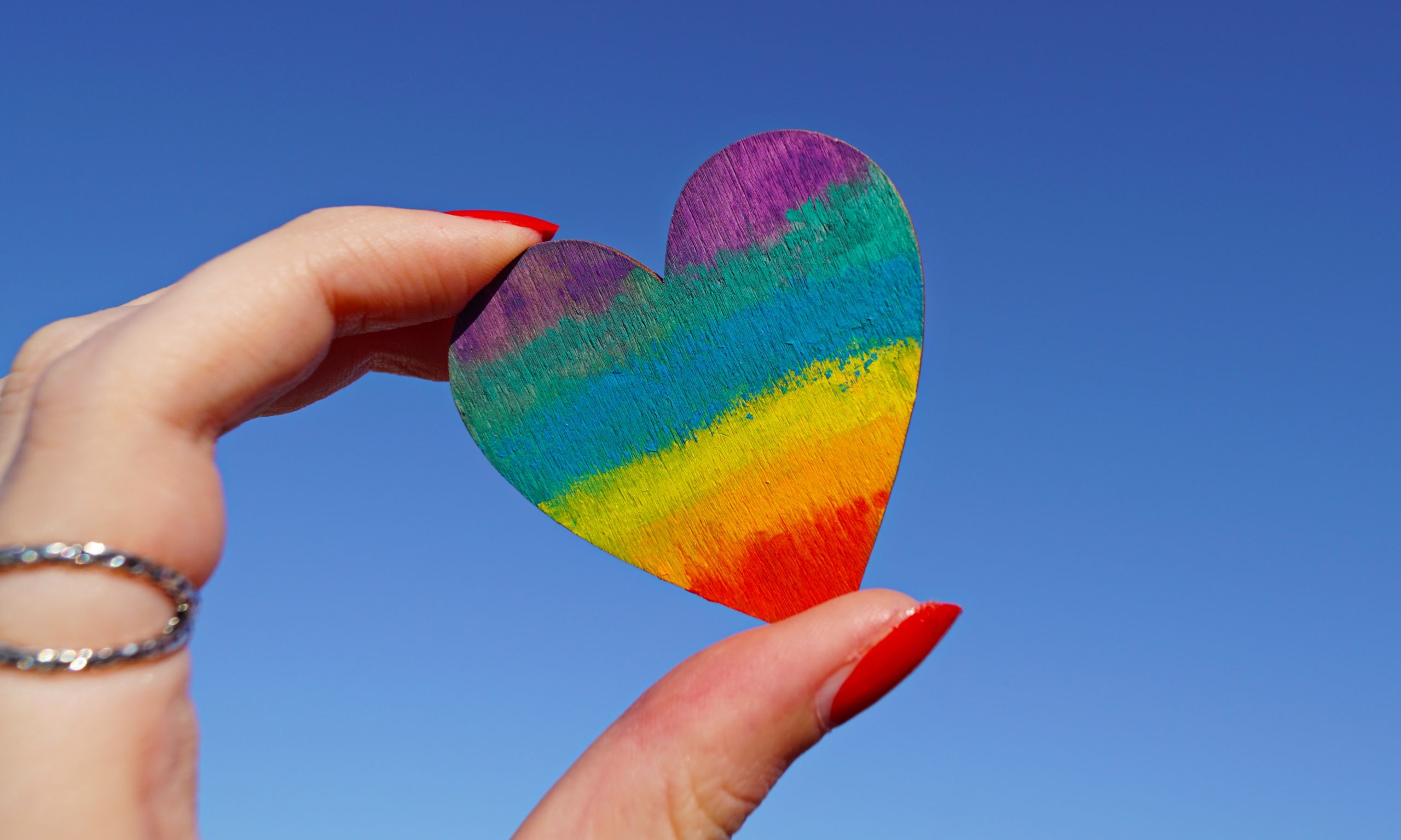 Photo of a person holding a multicolored heart deco. Happy Queer books reading!